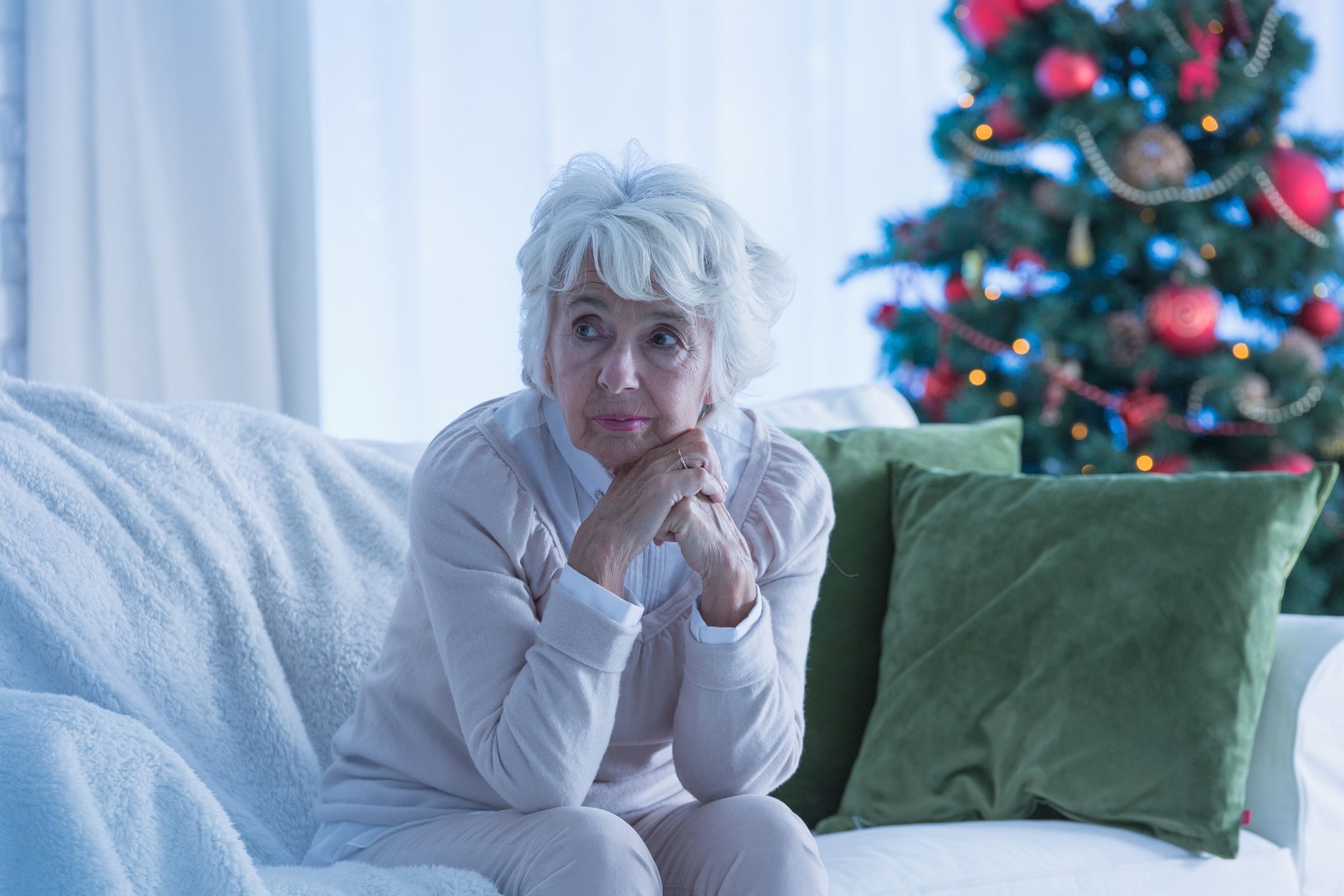 Senior woman sitting alone on sofa, christmas tree in background